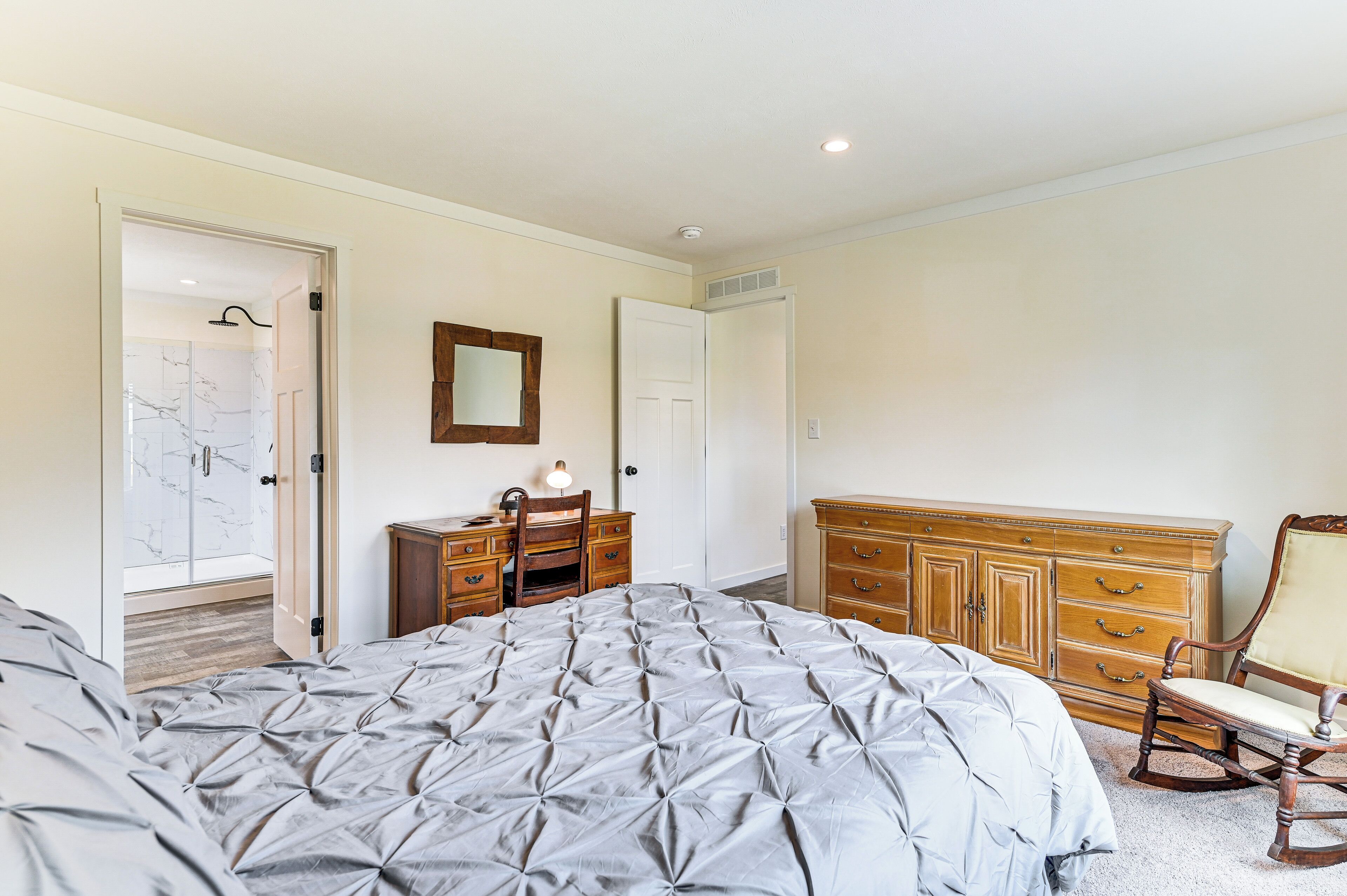 A bedroom with a large bed, wooden dresser, and a chair.