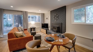 A modern living room with a sofa, a dining table set, a fireplace, and large windows. - Walk to Beach + Village: Bainbridge Island Gem! (Bainbridge Island)