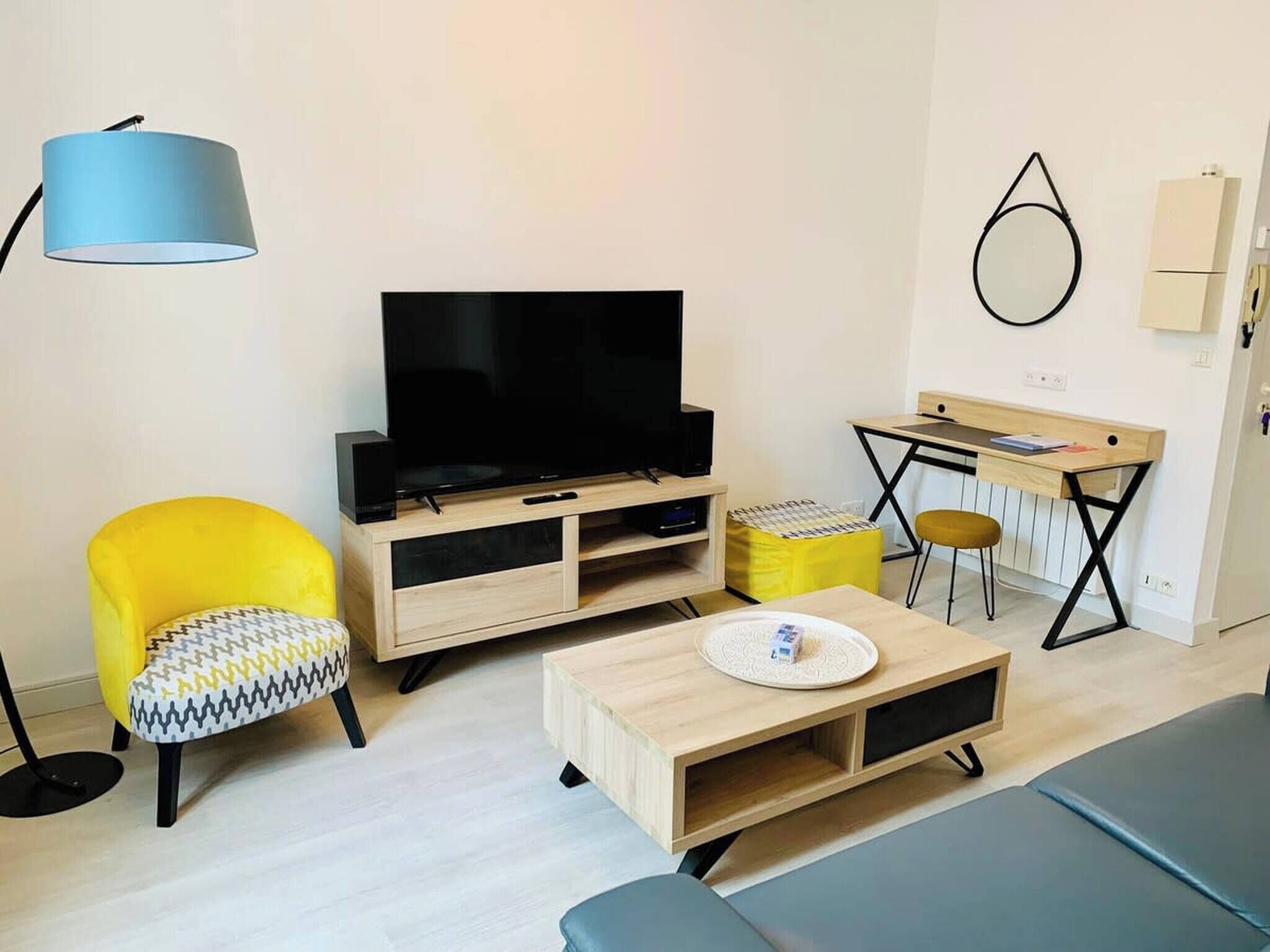 A modern living room with a flat-screen TV, a yellow armchair, a small wooden coffee table, and a desk with a chair.