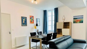 A modern living room with a black leather sofa, a dining table with chairs, a radiator, and artwork on the walls. - Le Grand Cloutiers, Centre Ville, LR135 (La Rochelle)