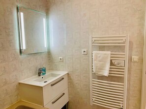 Ein Badezimmer mit einem weißen Waschbecken, einem Spiegel, einem Handtuchhalter und einer Toilette.