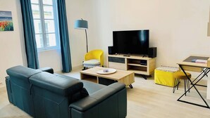 A modern living room with a black sofa, a yellow armchair, a TV on a wooden stand, and a small table with a lamp. - Le Grand Cloutiers, Centre Ville, LR135 (La Rochelle)