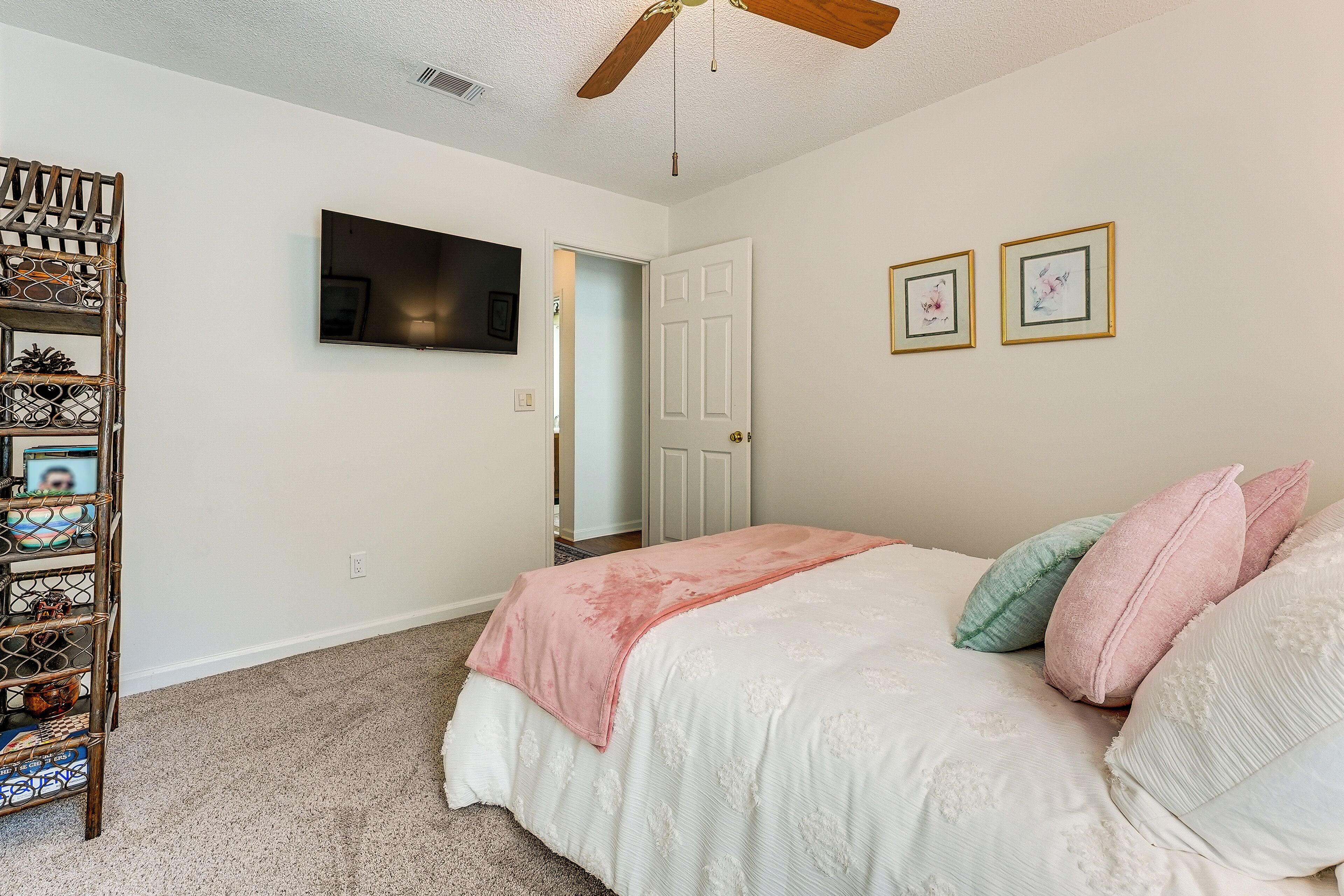 Un dormitorio con una cama, un televisor montado en la pared y una puerta que da a otra habitación.