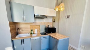 A compact kitchen with light blue cabinets, a wooden countertop, a built-in dishwasher, and a black microwave. - Le Petit Marché, Hypercentre, LR125 (La Rochelle)
