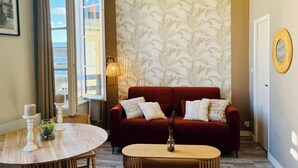 A cozy living room with a red sofa, a round wooden coffee table, and a patterned wallpaper. - Le Petit Marché, Hypercentre, LR125 (La Rochelle)