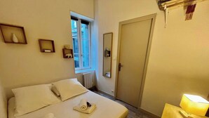 A hotel room with a bed, a window, a door, and a bedside table with a lamp. - Le Petit Marché, Hypercentre, LR125 (La Rochelle)