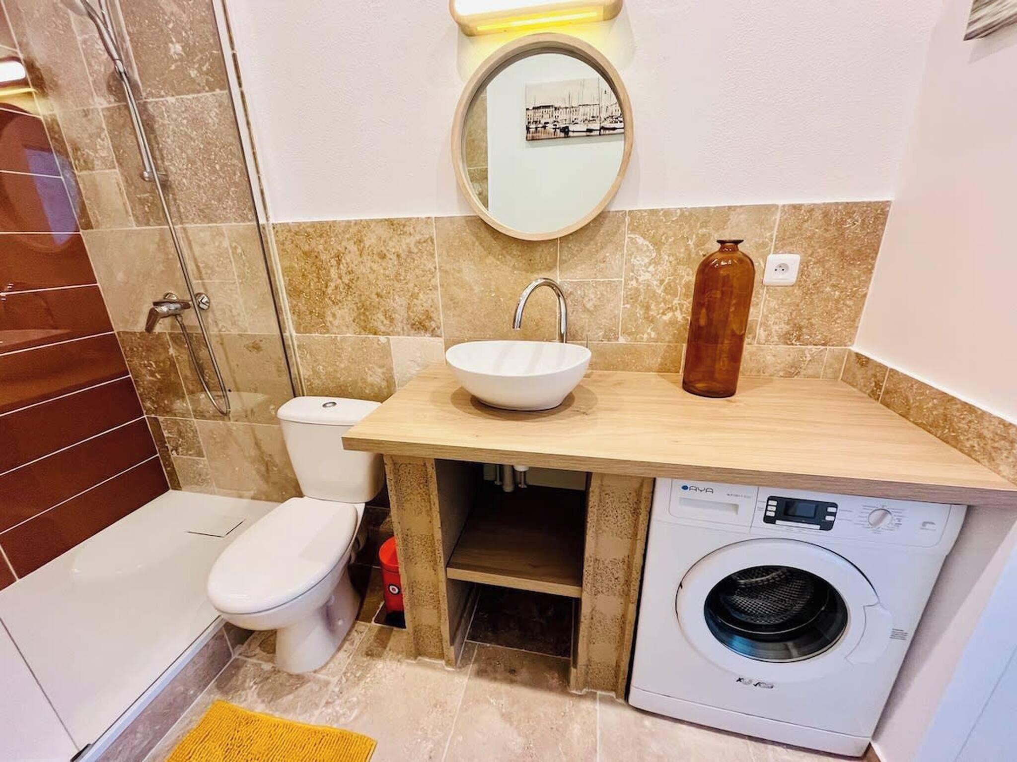 A compact bathroom with a white sink, a toilet, a washing machine, and a shower area.