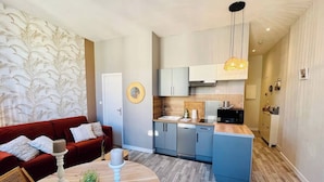A modern kitchen with a central island, a dining area with a round table, and a living room with a red sofa. - Le Petit Marché, Hypercentre, LR125 (La Rochelle)