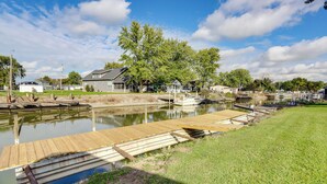 A riverside dock with a wooden walkway leading to a house with a large lawn and a boat docked nearby. - Walk to Lagoon Saloon! Chic Home on Nugent's Canal (Port Clinton)