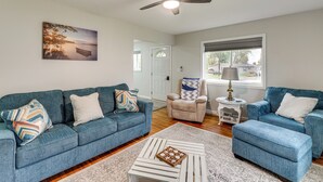 A living room with two blue sofas, a white coffee table, a ceiling fan, and a window with blinds. - Walk to Lagoon Saloon! Chic Home on Nugent's Canal (Port Clinton)