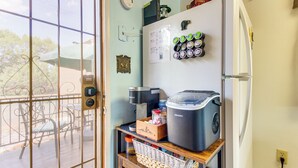 Et køkken med et køleskab, kaffemaskine og en stor beholder på bordet.