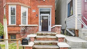 A red brick building with a black front door, a mailbox, and a small window with a sign above it. - Explore & Work! Stylish Washington Heights Duplex (Newburgh)
