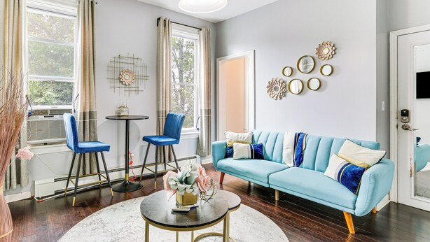A living room with a blue sofa, two blue chairs, a round coffee table, and a white door. - Explore & Work! Stylish Washington Heights Duplex (Newburgh)
