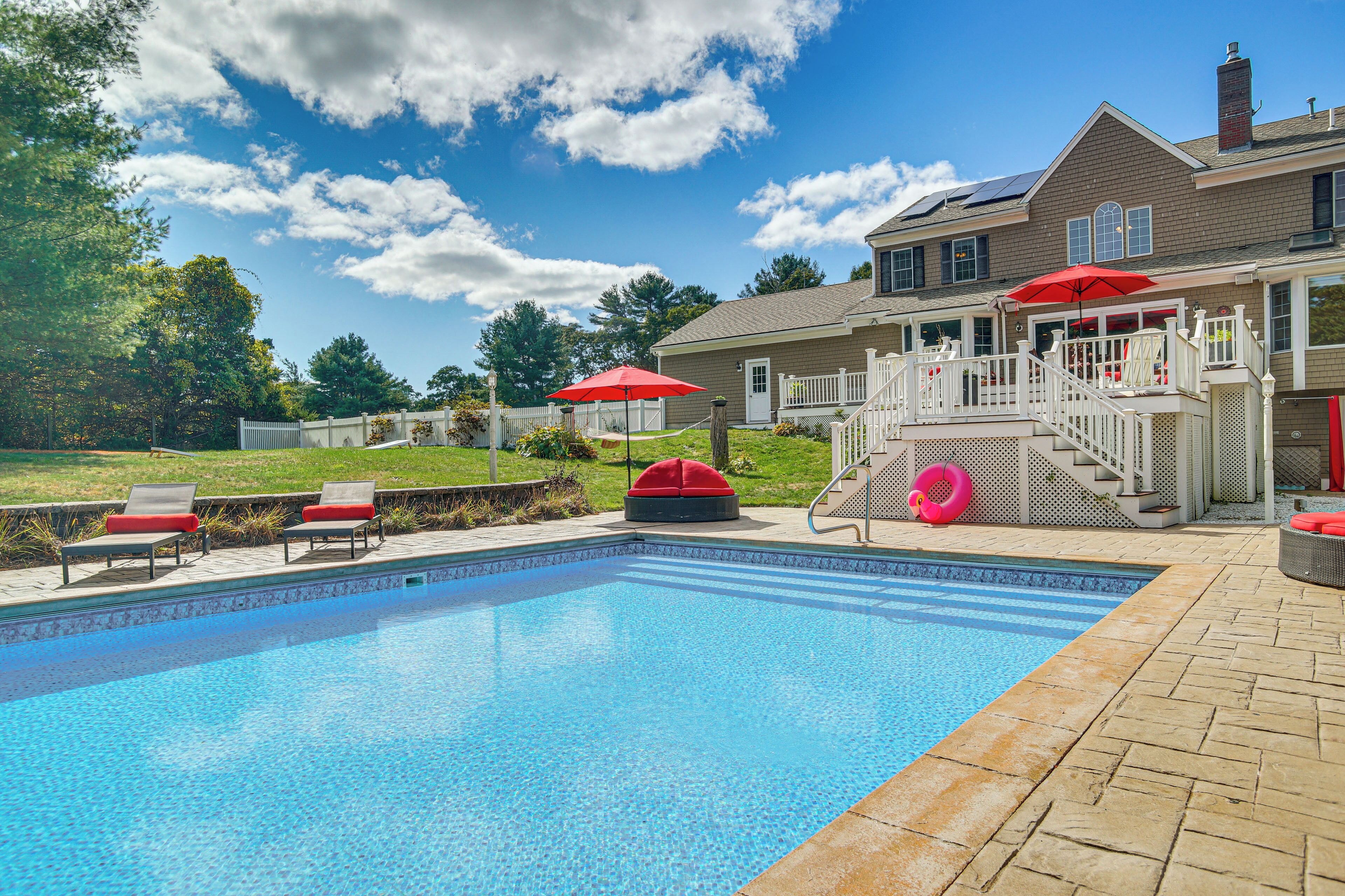 A swimming pool with lounge chairs and umbrellas, a covered deck, and a house in the background.
