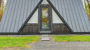 Une cabane en bois avec un toit triangulaire et une porte d’entrée dotée d’un panneau de verre.