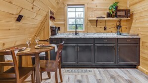 L’intérieur d’un chalet en bois comprend un espace cuisine avec des meubles de couleur sombre, un comptoir en granit et une fenêtre offrant une vue agréable.