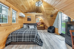 A wooden cabin bedroom with a bed, a chair, a sofa, a TV, and a window. - 5 Mi to Wine Trails: Finger Lakes Tiny Home (Ovid)