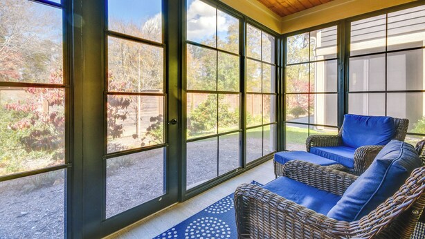 A sunroom with large windows, wicker furniture, and a wooden ceiling.