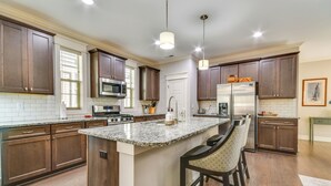 A modern kitchen with dark wooden cabinets, a granite countertop, stainless steel appliances, and a large island with bar stools.