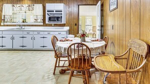 A kitchen with wooden paneling, white cabinets, a microwave, and a dining area with wooden chairs and a table.