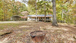 A rustic cabin with a porch, surrounded by trees and a fire pit.