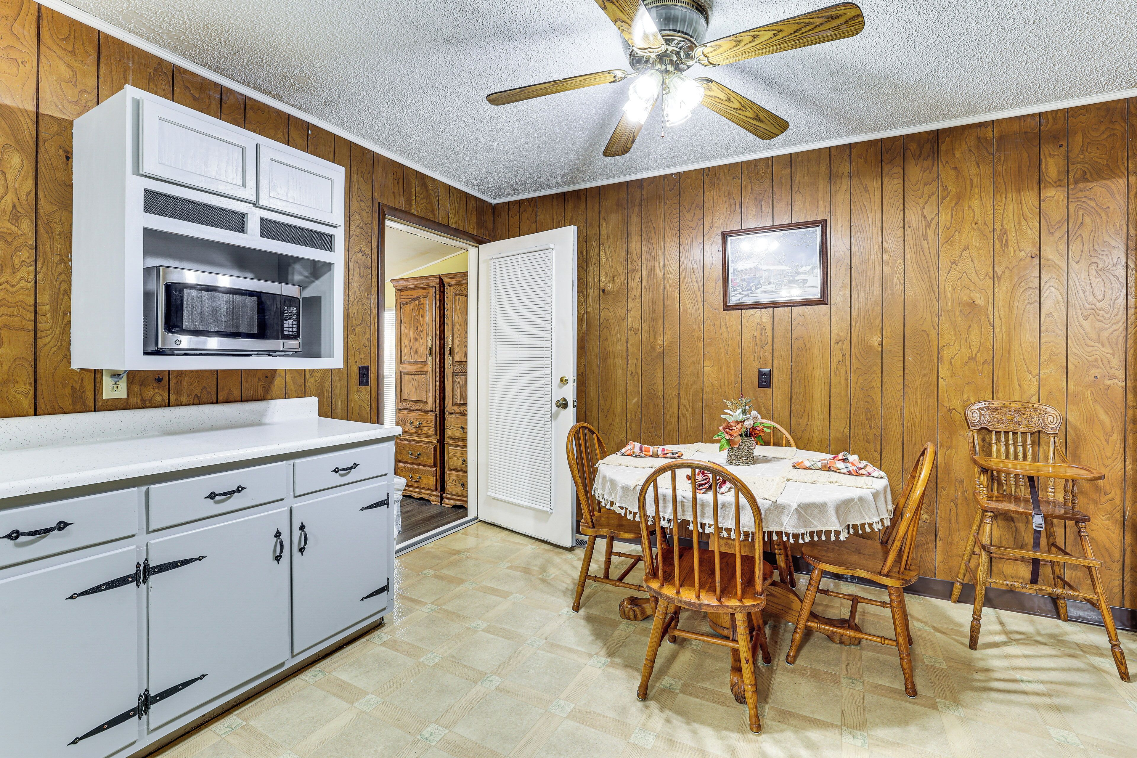 A kitchen with wooden paneling, a ceiling fan, a microwave, and a dining table with chairs.