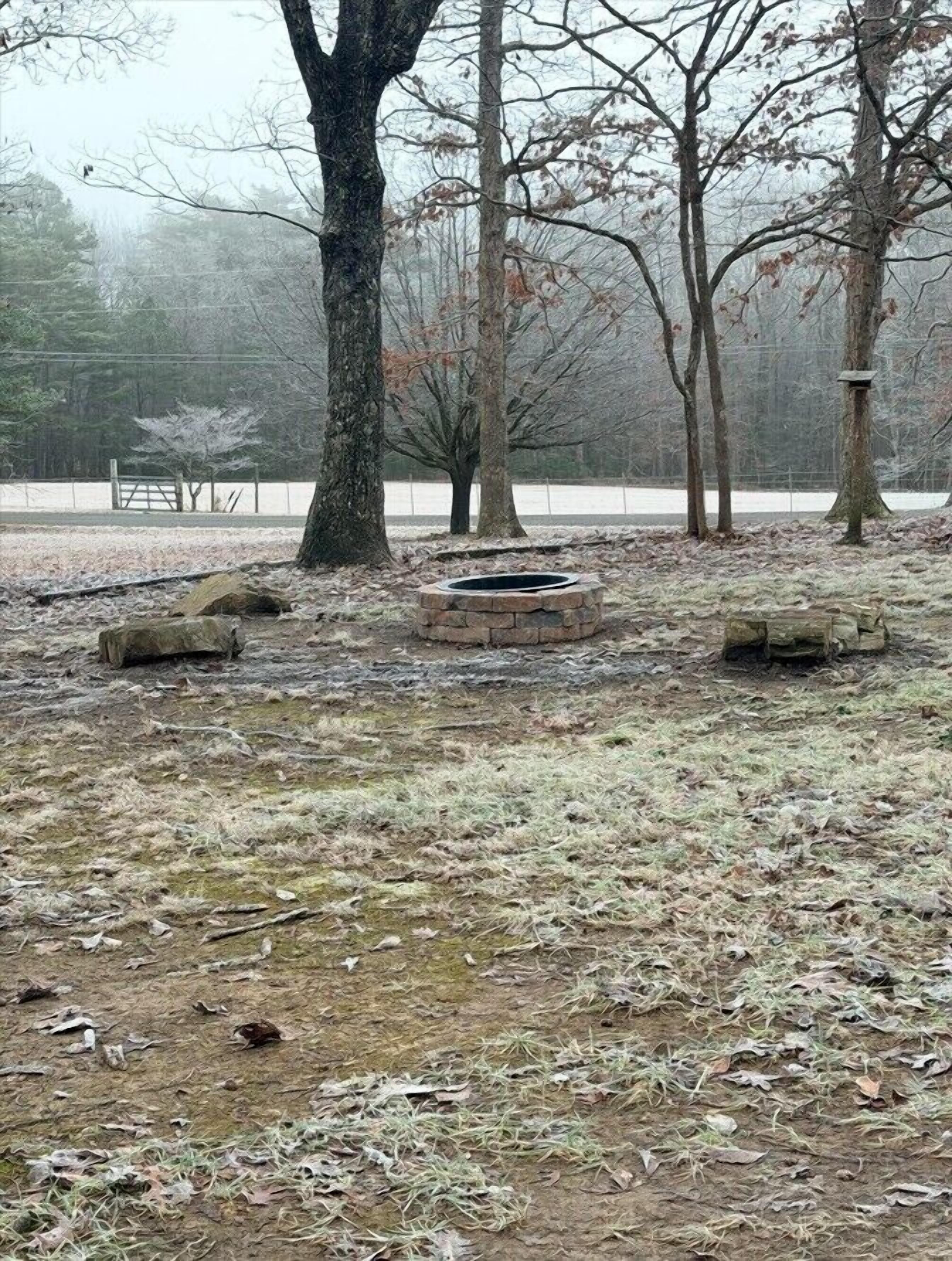 Un parc avec un foyer en pierre, entouré d’arbres et dont le sol est recouvert de neige.