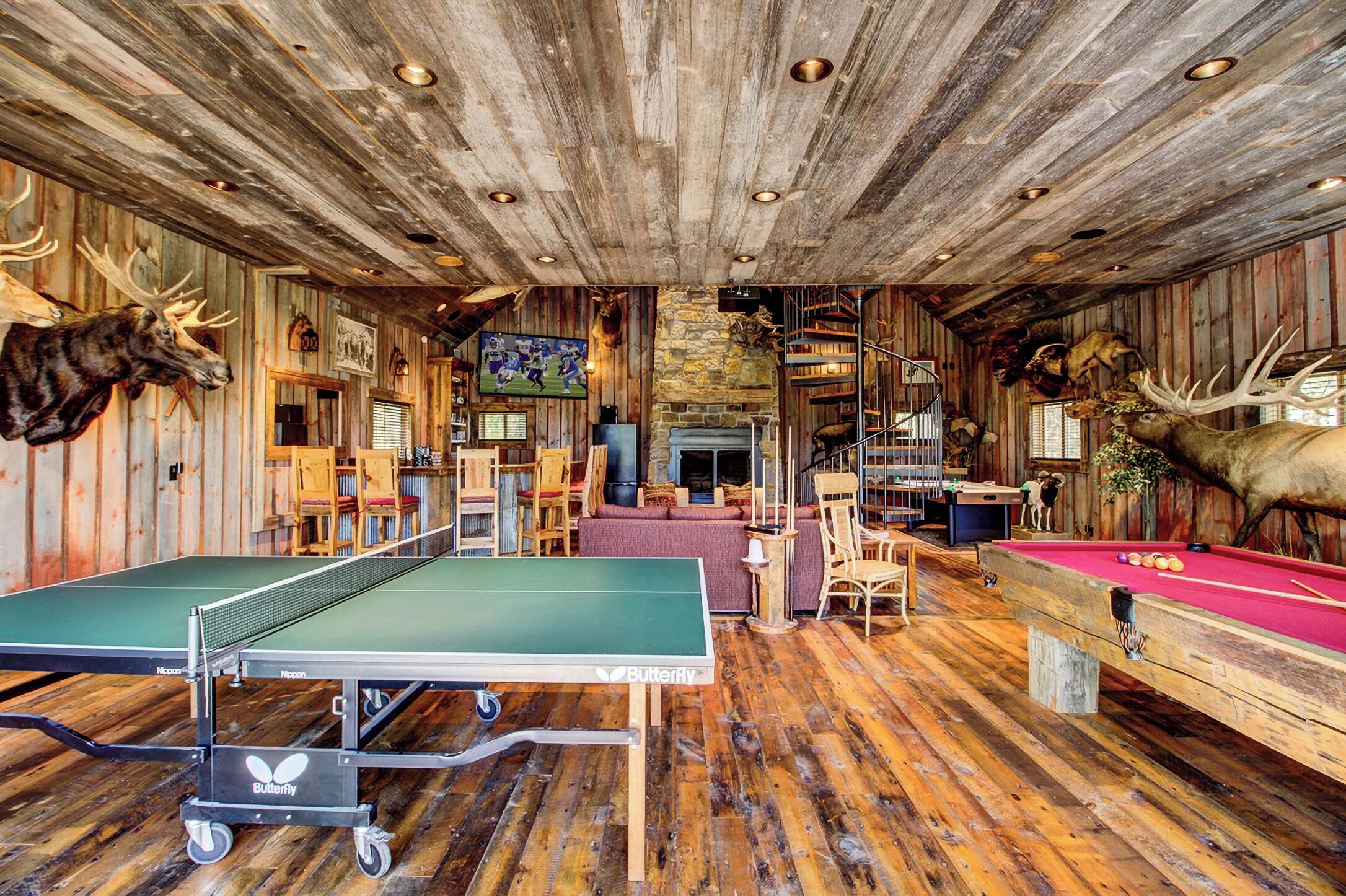 A rustic room with a ping pong table, pool table, and wooden walls adorned with animal heads.