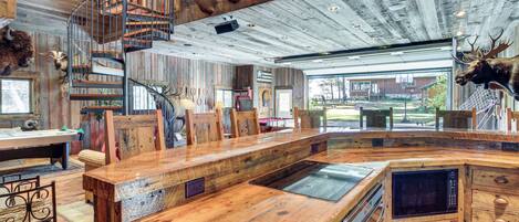 Un intérieur rustique avec un bar en bois, un escalier en colimaçon et des têtes d’animaux fixées au mur.