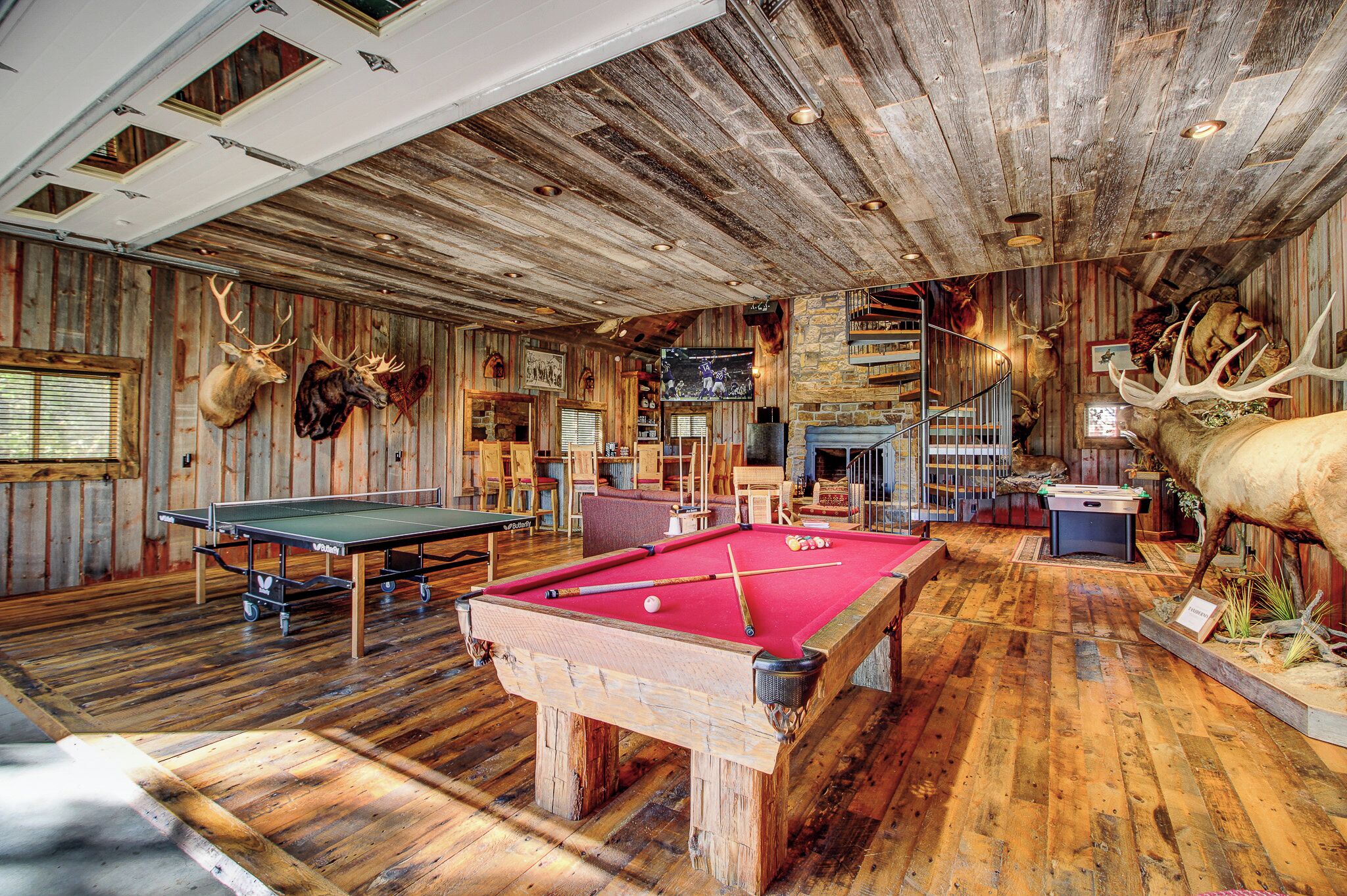 A rustic room with a pool table, wooden walls, and mounted animal heads.
