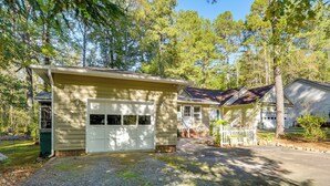 A two-story house with a garage, surrounded by trees and a gravel driveway.
