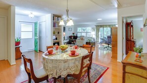 A dining area with a round table, chairs, and a chandelier. There is a bookshelf and a sofa in the background.