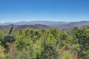 A mountainous landscape with dense forest in the foreground and a clear blue sky.