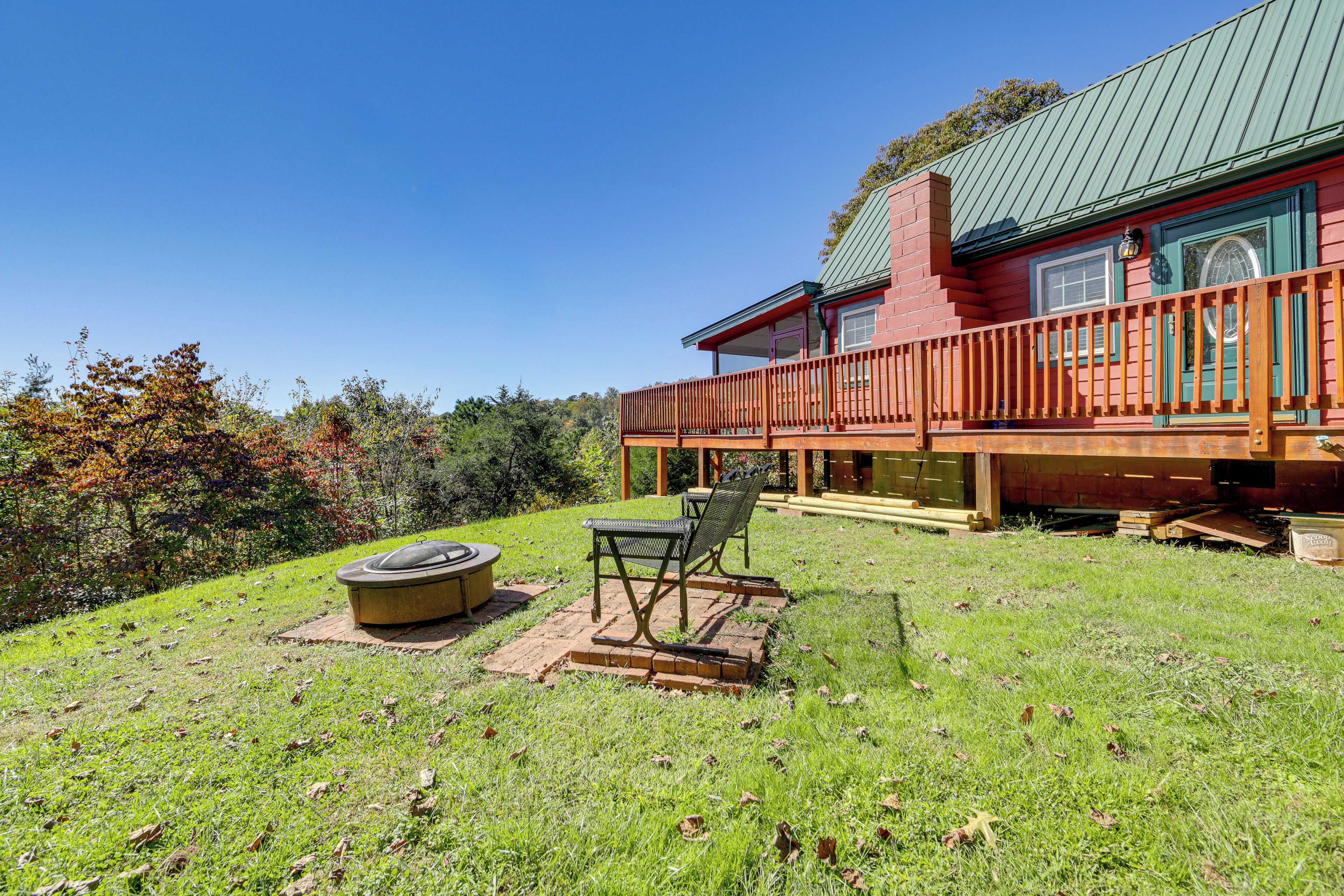 A red wooden house with a green roof, a deck, and a fire pit.