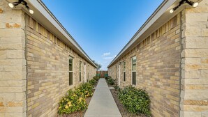 A corridor with brick walls and a concrete path flanked by small bushes and pebbles.