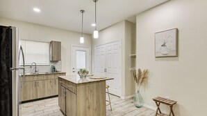 A modern kitchen with wooden cabinets, a central island, pendant lighting, and a vase with pampas grass.