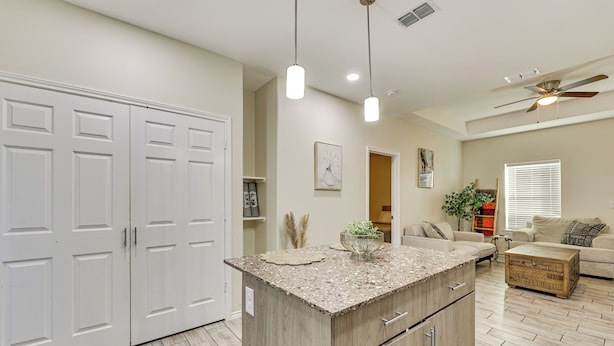 A kitchen with a central island, white double doors, pendant lights, and a ceiling fan.