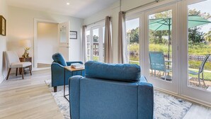 A modern living room with a sofa, a chair, a small table, and a view of the outdoors through large windows. - Boat Dock & Yard: Waterfront Okeechobee Retreat (Okeechobee)