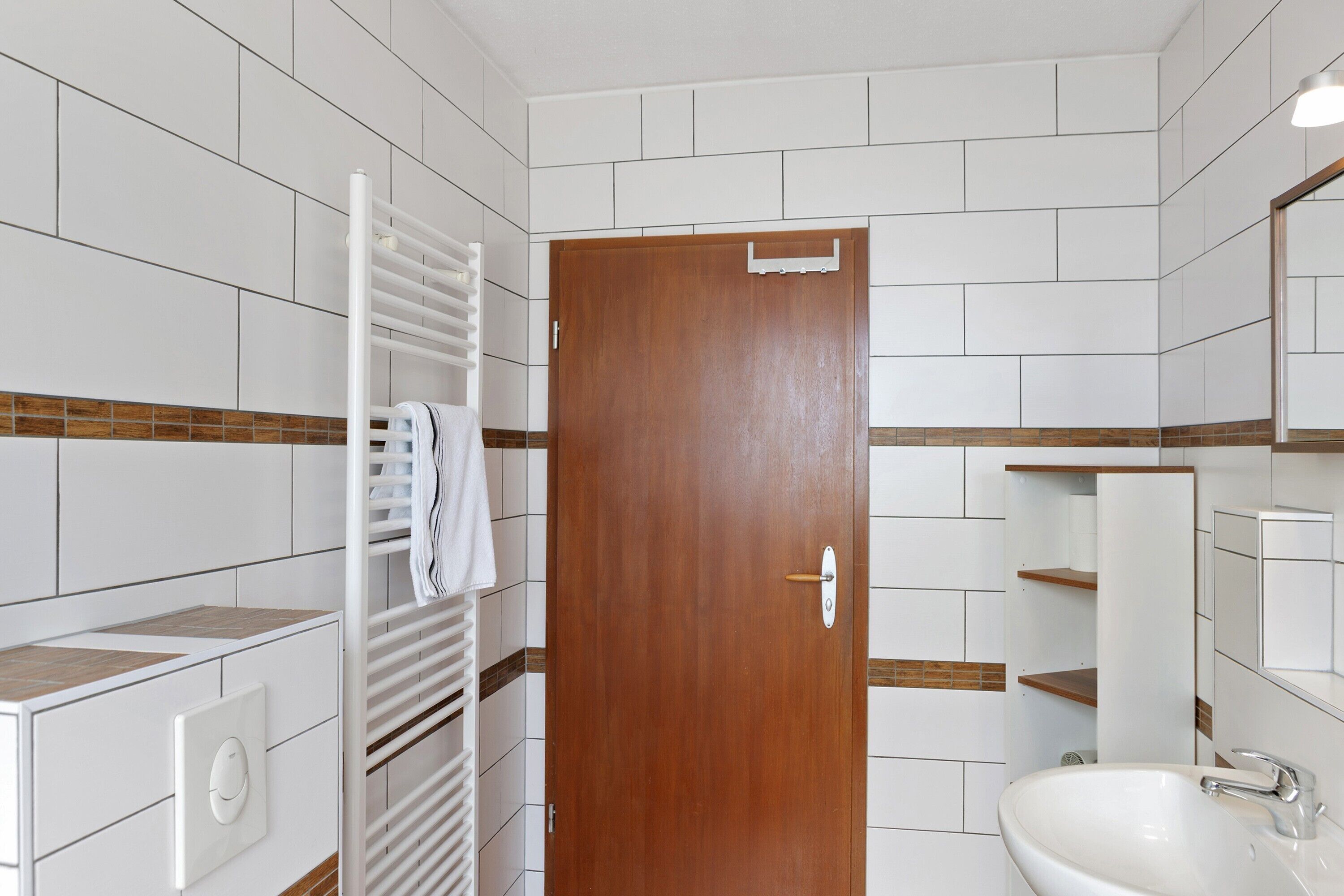 A bathroom with a white sink, a mirror, a towel rack, and a wooden door.