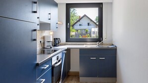 A compact kitchen with a built-in oven, a coffee maker, and a window overlooking a house. - Apartment 'Vollmarshausen' with Shared Garden and Wi-Fi (Lohfelden)