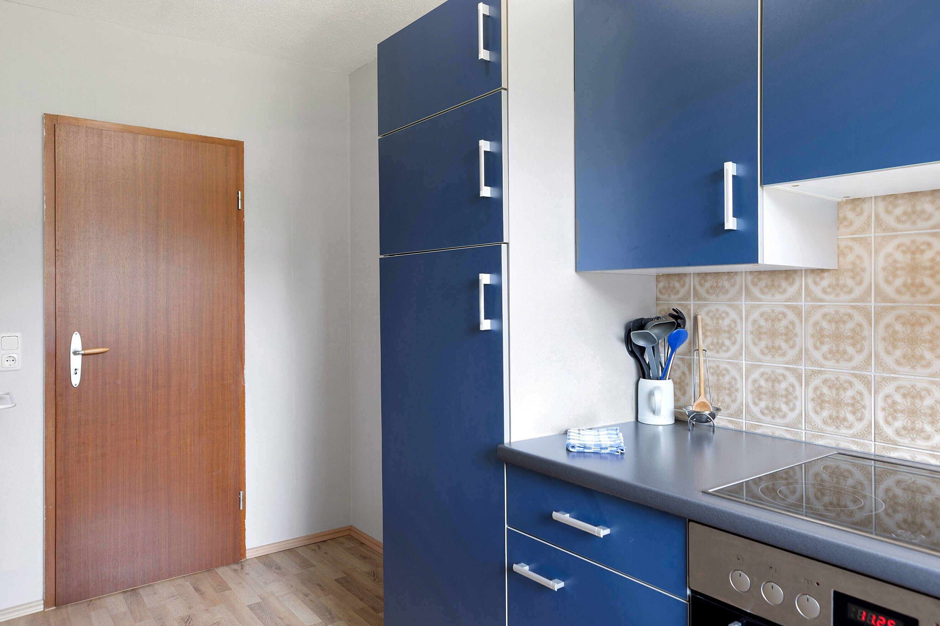 A kitchen with blue cabinets, a wooden door, and a tiled backsplash.