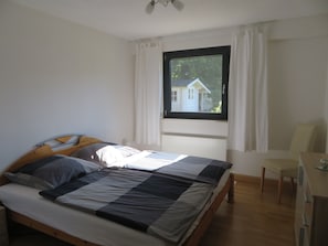 A bedroom with a bed, a window, a chair, and a desk.