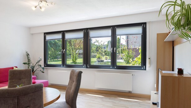 A modern living room with a large window, a dining table, a sofa, and a chair. - Apartment 'Vollmarshausen' with Shared Garden and Wi-Fi (Lohfelden)