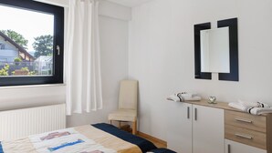 A bedroom with a bed, a chair, a dresser, a mirror, and a window with curtains. - Apartment 'Vollmarshausen' with Shared Garden and Wi-Fi (Lohfelden)