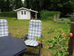 A garden with a small white shed, two checkered chairs, and a table.