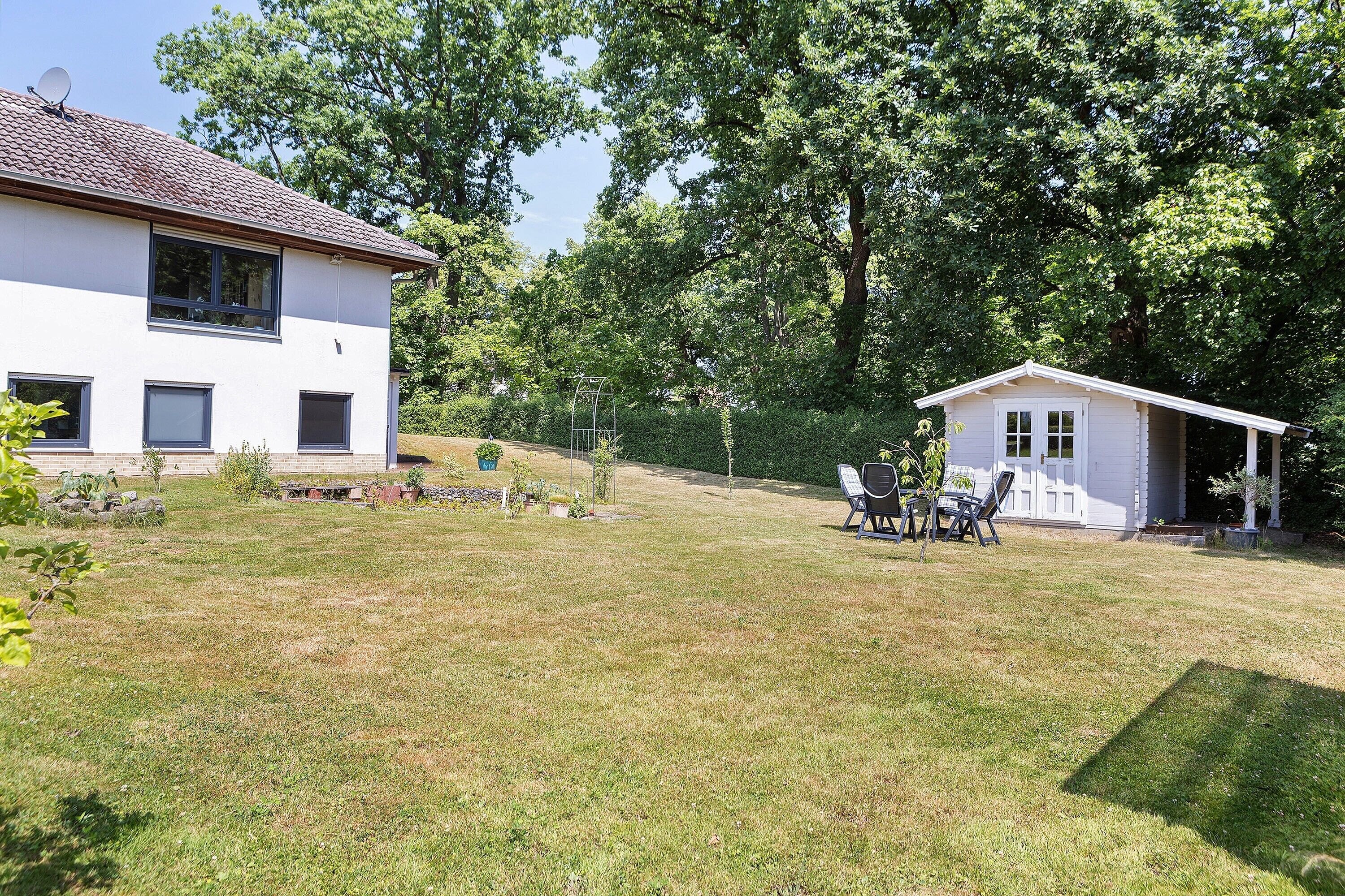A white house with a garden, a small shed, and a bench.