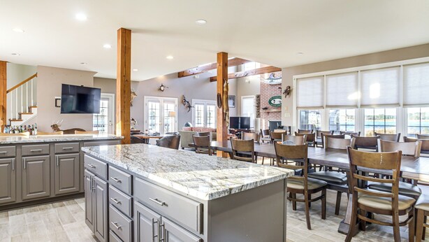 A spacious kitchen with granite countertops, wooden chairs, and a large dining table.