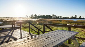 A wooden deck with picnic tables overlooking a grassy area and a body of water.