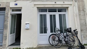 A two-story building with a beige facade, white shutters, and a balcony with plants. There are bicycles and an electric scooter parked in front. - Le bonpland, centre ville, LR122 (La Rochelle)