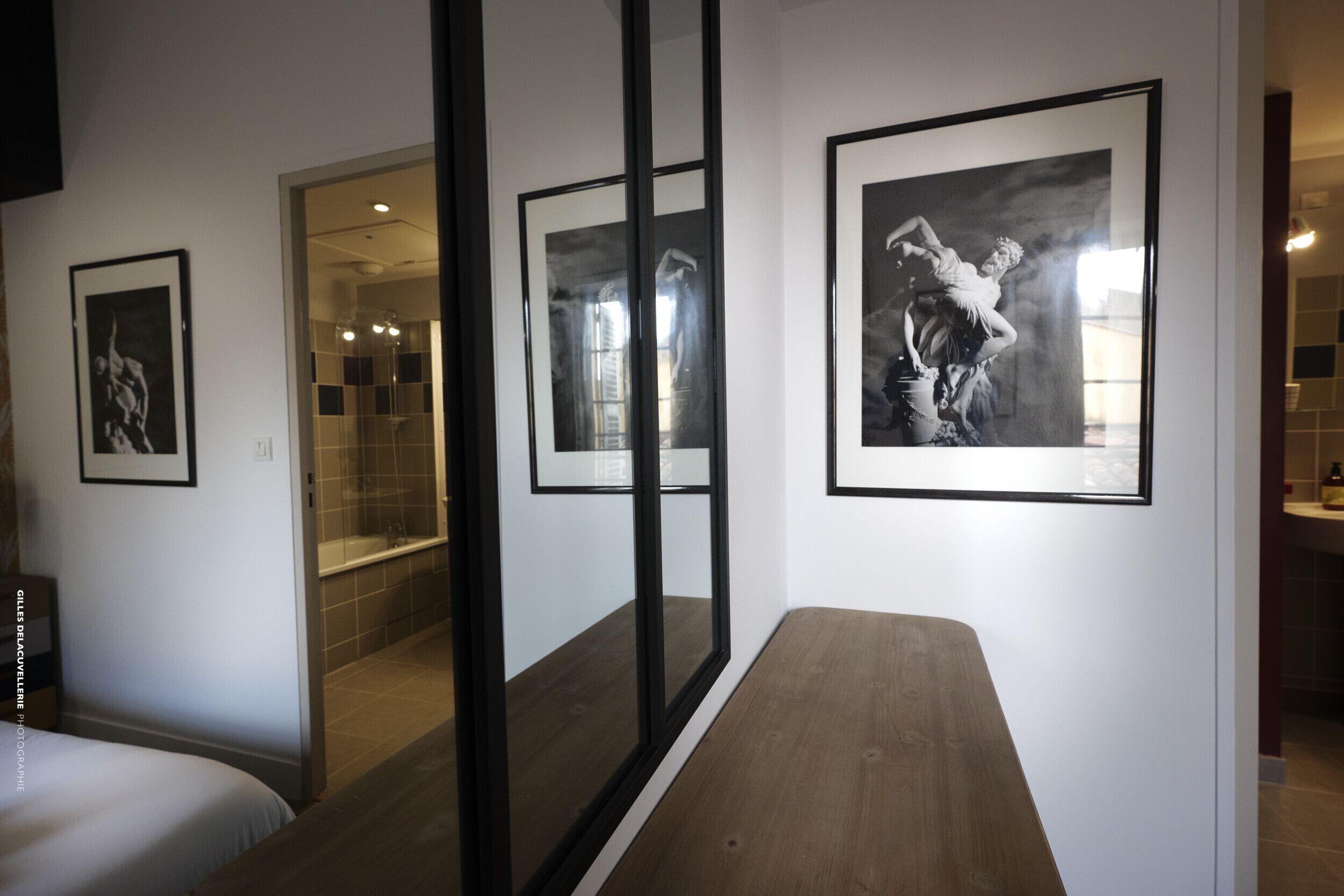 Habitació d'hotel amb un llit, una banca de fusta i tres fotografies en blanc i negre amb marc a la paret.